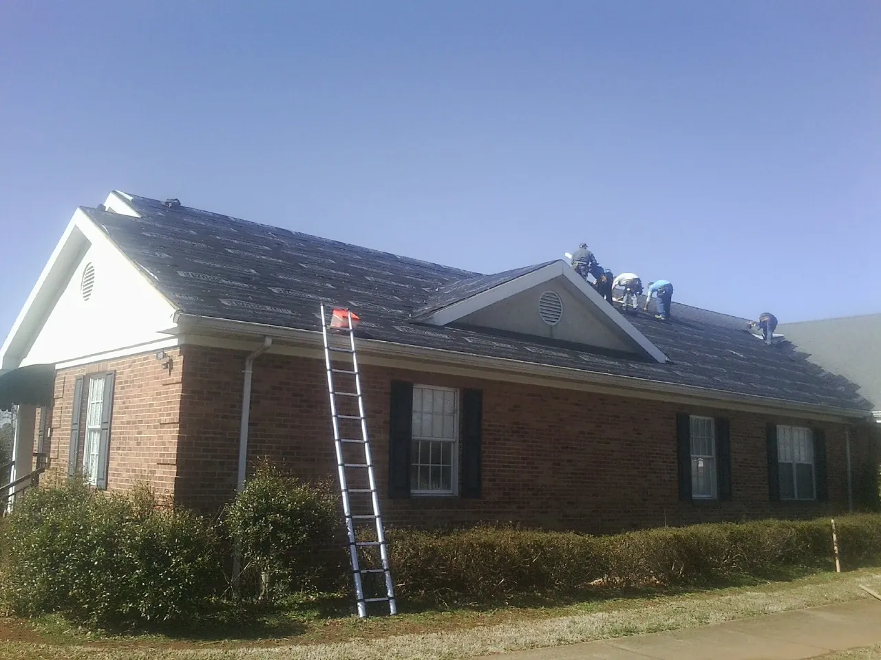 Crew tearing shingles off a brick ranch roof with a ladder set — Emergency Roof Repair work by our crew in Morrison